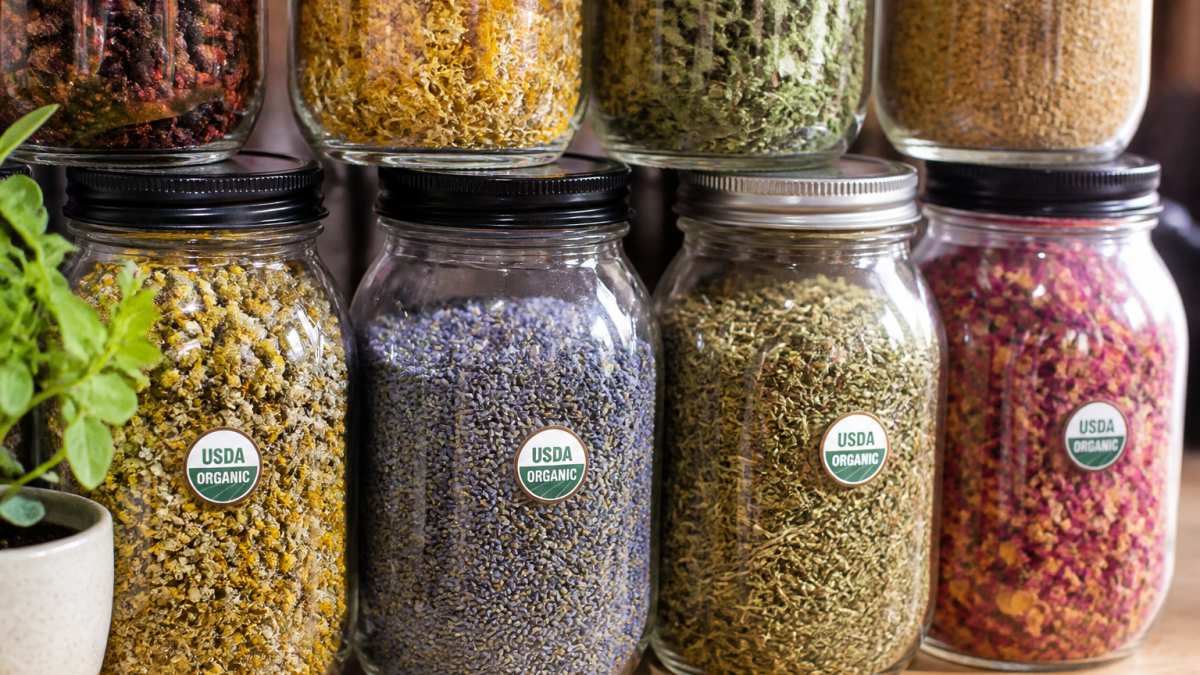 Close-up of dried herbs and spices in glass jars showing vibrant colors and clear labeling of organic certification marks on containers