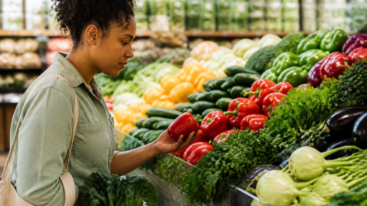 Person selecting fresh colorful vegetables and fruits from produce display in bright grocery store lighting, examining items with care